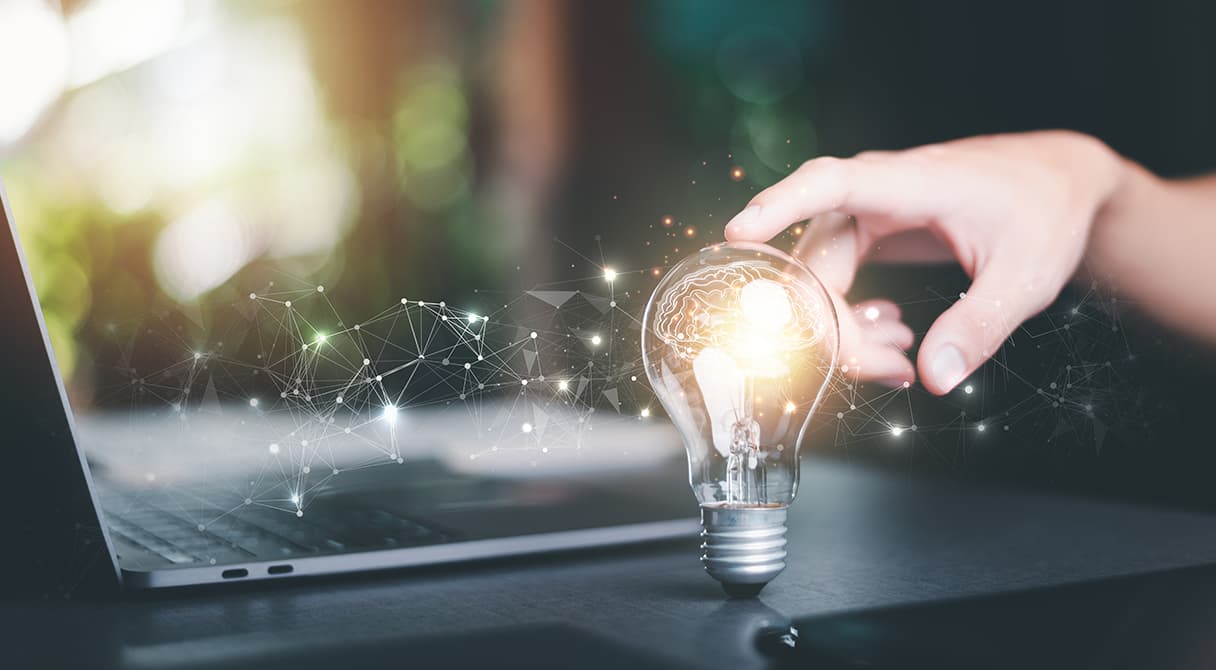 Világító izzó laptop mellett, amely a ZÉG digitális tervezési hátterét, mérnöki gondolkodását és korszerű műszaki megoldásait szimbolizálja.