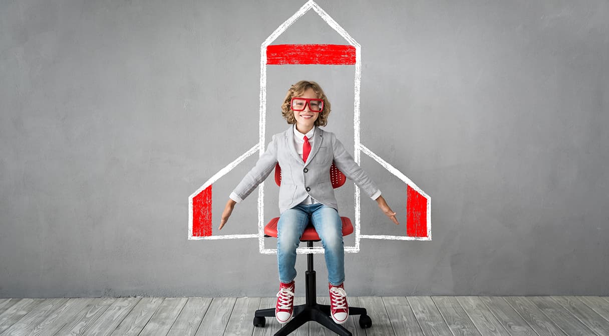 Rakétát formázó rajz előtt ülő gyermek, amely a fejlődést, az előrelépést és a jövőbe mutató szemléletet szimbolizálja.