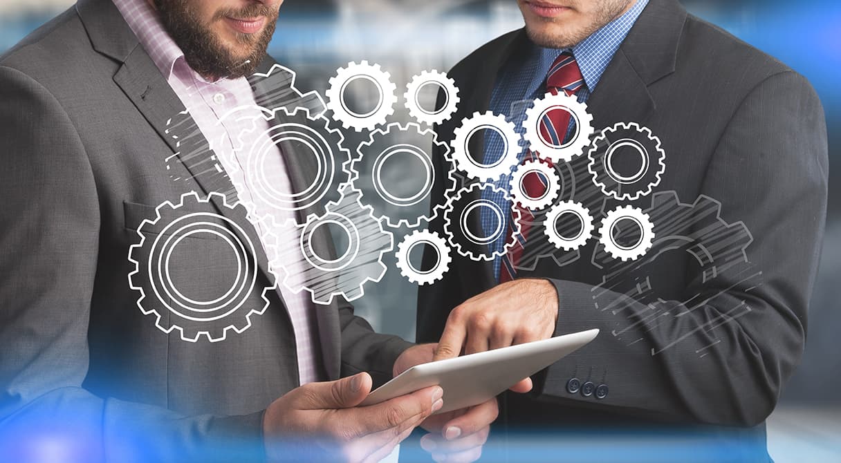 Két szakember táblagépet használ, fogaskerekeket ábrázoló grafikai elemekkel, az üzemeltetési és karbantartási folyamatok összehangolt működését jelképezve.