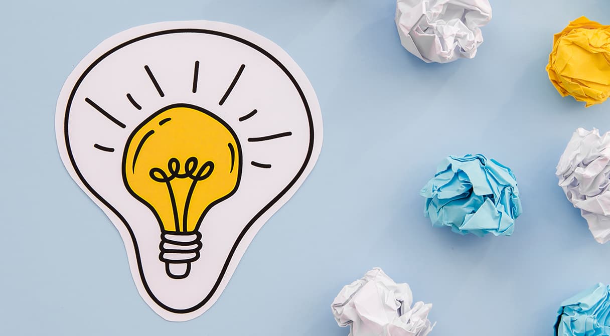 A ZÉG innovatív szemléletét jelképező papír izzó és kreatív ötleteket szimbolizáló összegyűrt papírlapok világoskék háttéren.