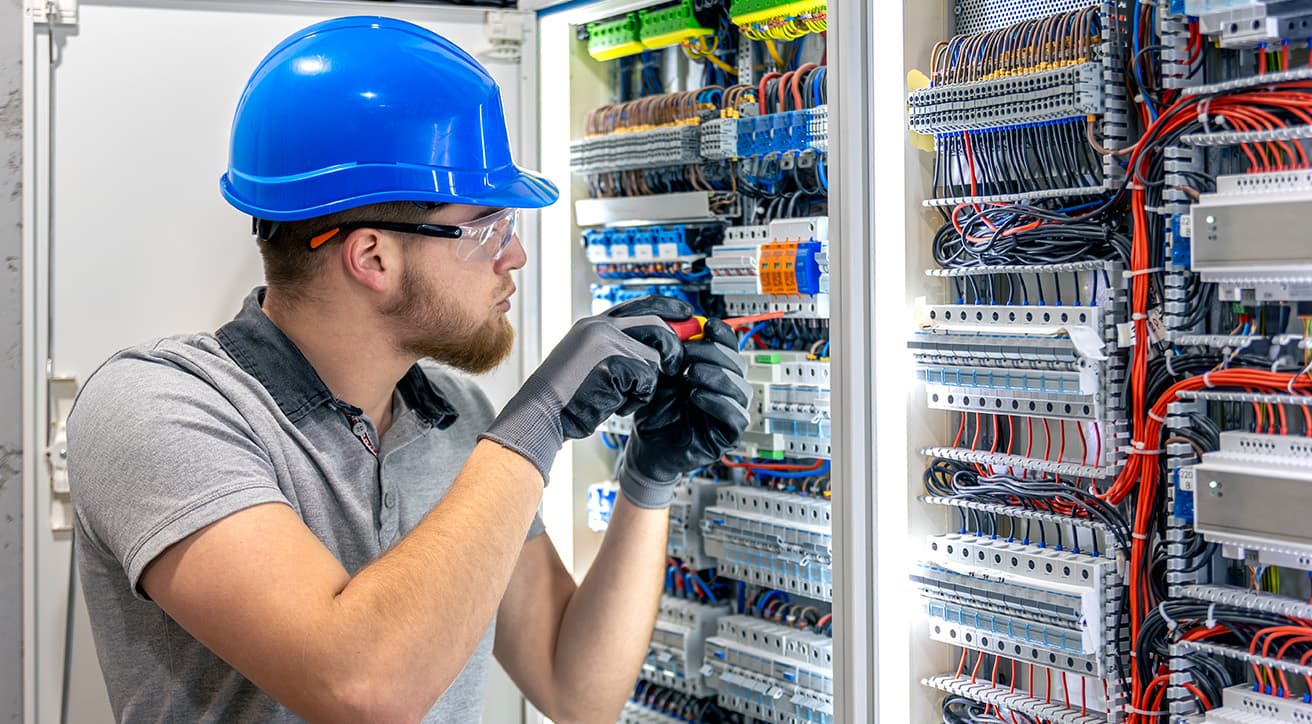 Villanyszerelő dolgozik egy elektromos kapcsolószekrényen, korszerű villamos hálózat kiépítése közben.