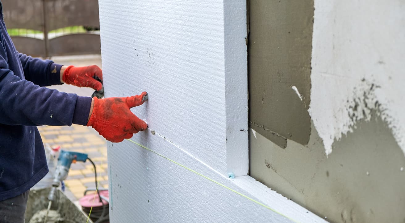 Munkás homlokzati hőszigetelő lapokat illeszt egy épület falára felújítás és energetikai korszerűsítés közben.