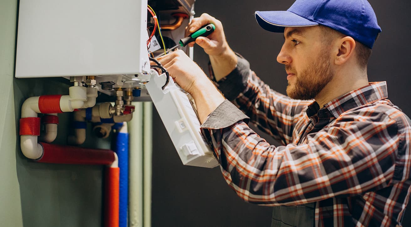 Szakember fűtési rendszer csőhálózatát és szelepeit ellenőrzi egy beltéri gépészeti falon.