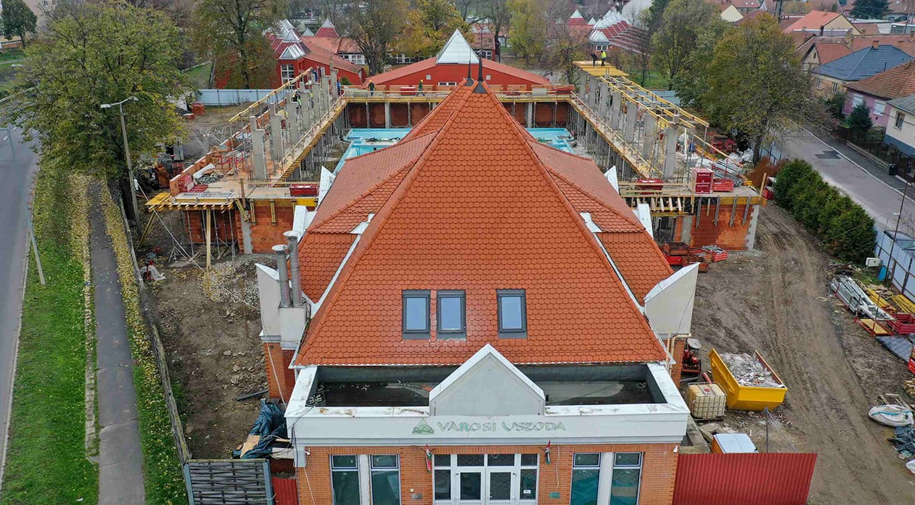  Légifelvétel építés alatt álló középületről, a közintézményi kivitelezés szervezett munkafolyamatait bemutatva.