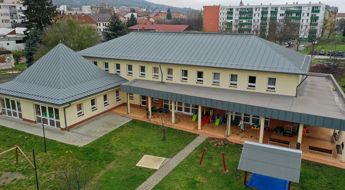 Légifelvétel a bővített bölcsőde épületéről udvarral, fedett terasszal és zöldfelülettel.