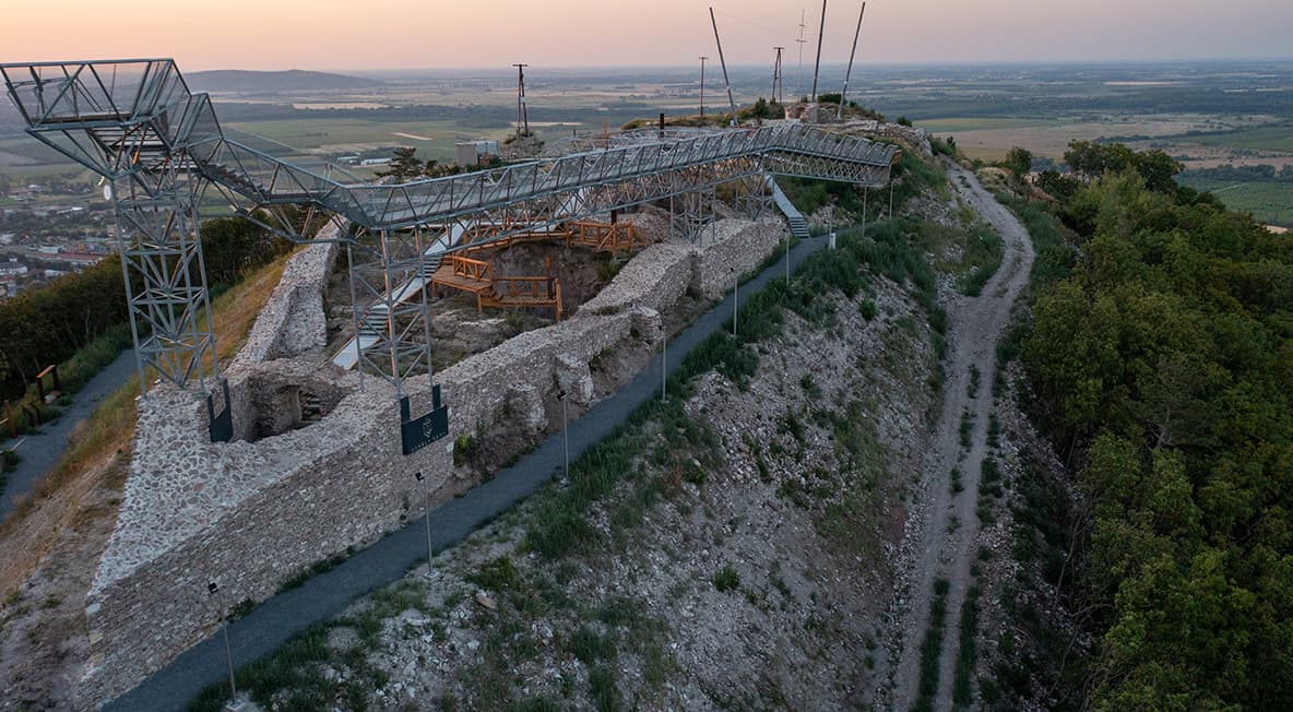 Légifelvétel a várhegyi kilátó sétányról és a részben helyreállított várfalakról naplemente idején.