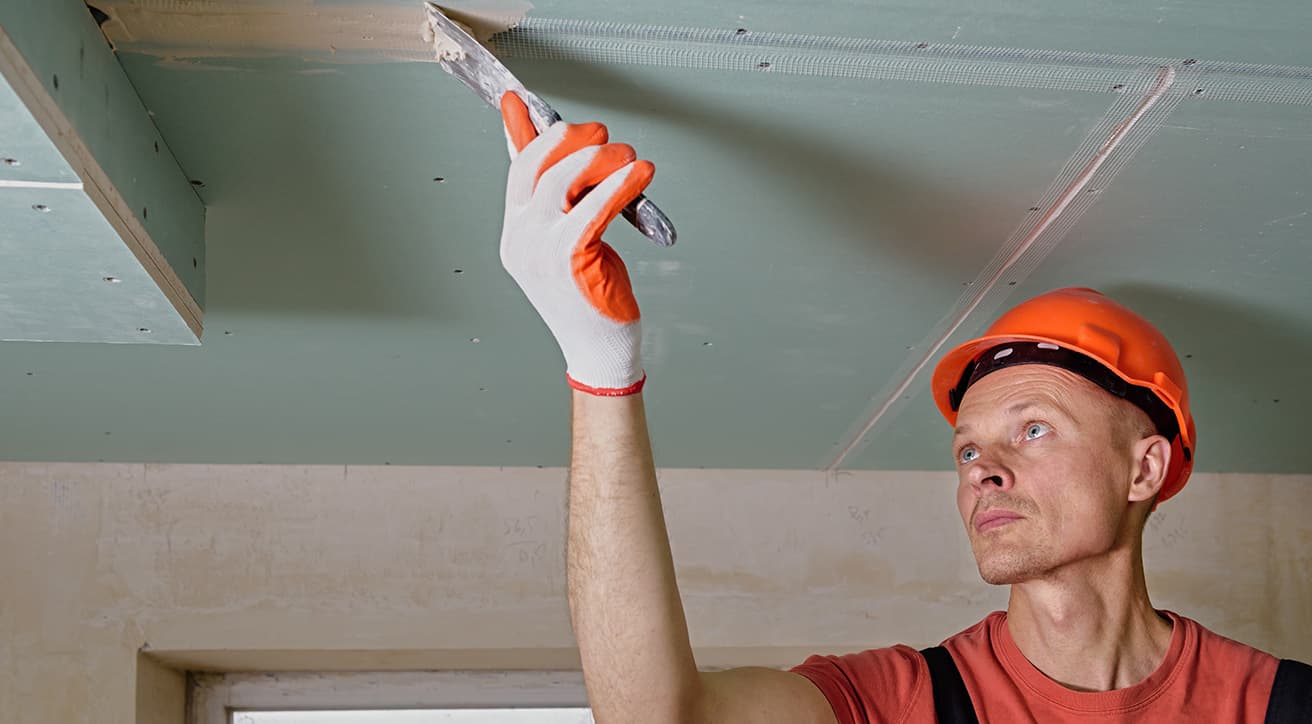Szakember glettel és simít egy beltéri gipszkarton mennyezetet, befejező belsőépítészeti munkák közben.