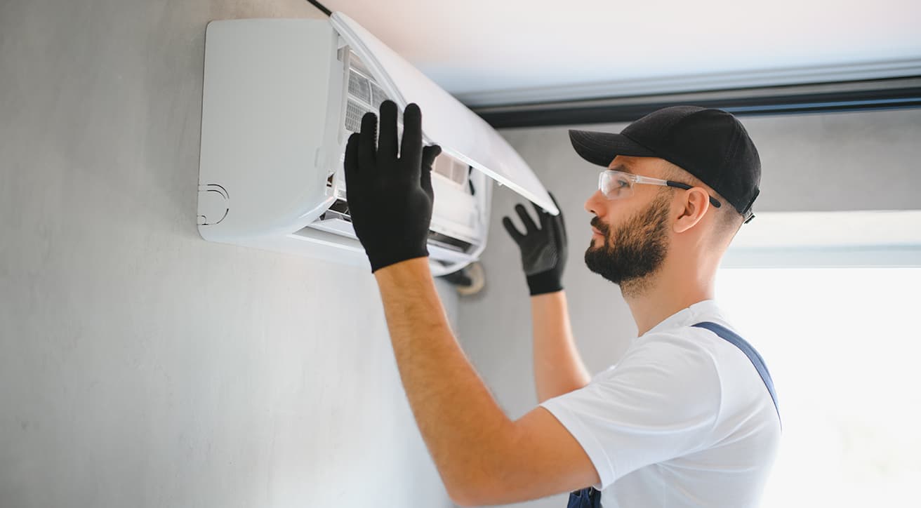 Szakember falra szerelt beltéri klímaberendezést tisztít és ellenőriz karbantartás közben.