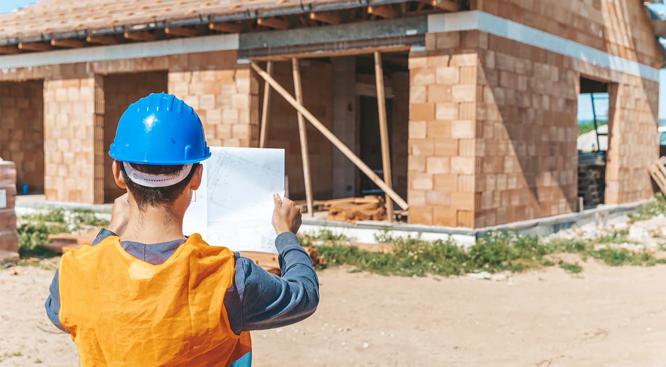 Építés alatt álló téglaház szerkezete, falazott főfalakkal és készülő tetőszerkezettel.