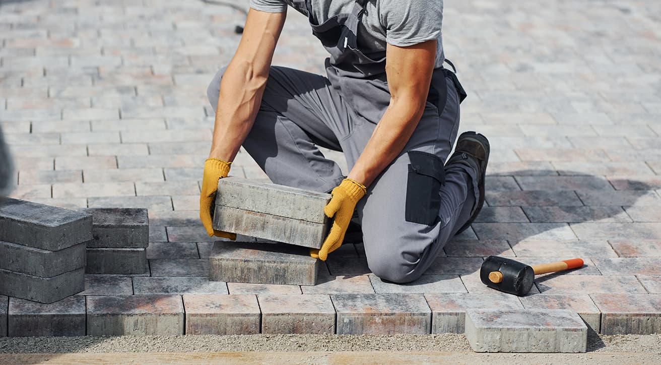 Munkás térköveket helyez le egy kültéri burkolt felületen, előkészített alépítménnyel és gumilapáccsal.